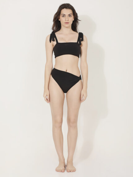 Front of a women in a classic square neck shouldr tie up bikini top and a twisted knotted bikini bottom. women in a two piece black bikini.